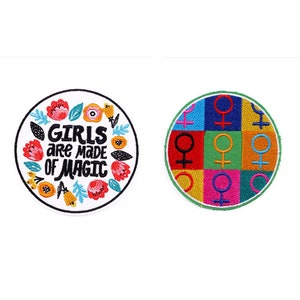 Könnte beinhalten: Zwei gestickte Bügelbilder. Ein Patch ist weiß mit einem floralen Rand und dem Text "Girls are made of magic". Der andere Patch ist ein farbenfrohes Patchwork-Design mit einem sich wiederholenden weiblichen Symbol.