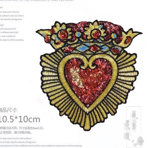 Pode incluir: Um remendo bordado em forma de coração vermelho e dourado com uma coroa no topo. O remendo mede 10,5 cm por 10 cm.