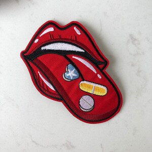 May include: Red embroidered patch of a tongue with pills and a star on it.