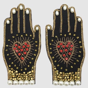 May include: Two black fabric hands with gold and red bead embellishments. Each hand has a red heart in the center with gold bead accents. The hands are surrounded by a row of white pearl beads.
