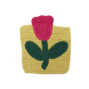 May include: A yellow crocheted coaster with a pink and green flower design. The flower has a single stem and two leaves.