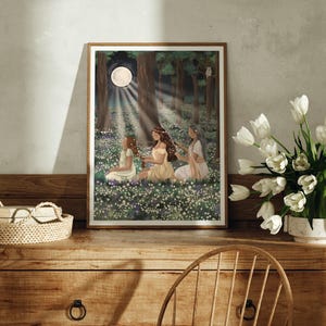 May include: A framed art print depicts three figures in a forest clearing, bathed in moonlight. The artwork features a serene scene with figures in flowing gowns amidst a field of white flowers, with a full moon and trees in the background.