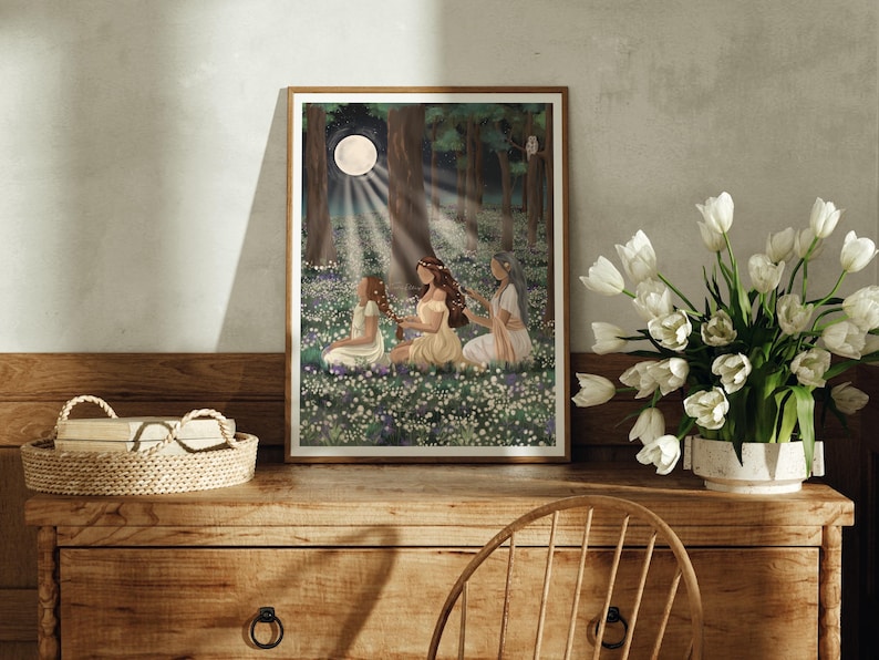 May include: A framed art print depicts three figures in a forest clearing, bathed in moonlight. The artwork features a serene scene with figures in flowing gowns amidst a field of white flowers, with a full moon and trees in the background.