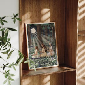 May include: A framed art print depicting three figures in a moonlit forest clearing. The artwork features a full moon, rays of light, and a field of white flowers. The figures are dressed in flowing gowns, with long hair, and are seated in the flowers.