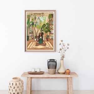 May include: A framed illustration of a woman sitting cross-legged on a rug in a room filled with plants. The woman is wearing a green dress and has headphones on. The room has a window with a view of trees and a bookshelf filled with books.