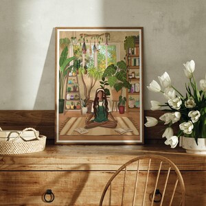 May include: A framed illustration of a woman meditating in a room filled with plants. The woman is wearing a green shirt and has long brown hair. The room has a window with a view of trees and a bookshelf filled with books.