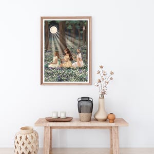 May include: A framed art print depicts three figures in a moonlit forest clearing. The artwork features a full moon, dappled light, and a field of flowers. The figures are seated, wearing flowing dresses, and appear to be in a moment of quiet contemplation.
