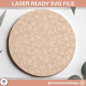 May include: A round wooden coaster with a laser-cut design of many ghosts. The ghosts are outlined in a light brown color and have simple facial features.