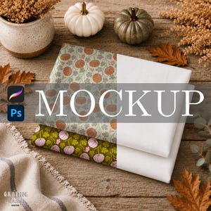 May include: Two folded pieces of fabric featuring pumpkin patterns. The top fabric has orange pumpkins on a light green background, while the bottom fabric has light purple pumpkins on a dark olive green background. Both have a solid white section.