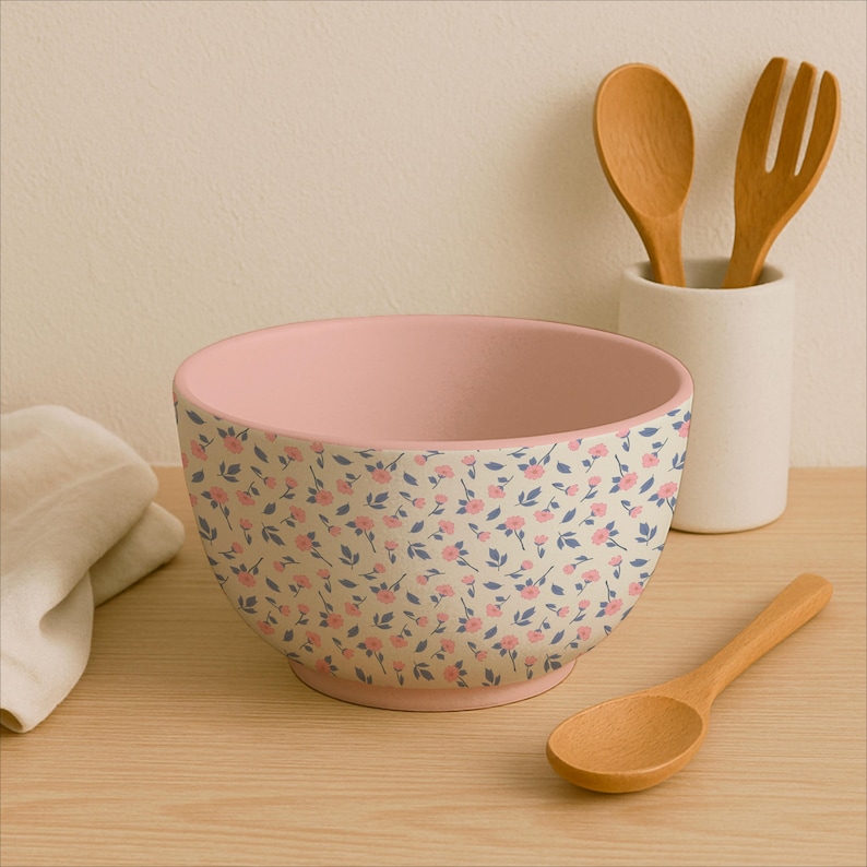 Puede incluir: Un cuenco de cer&aacute;mica con interior rosa y un estampado floral de flores rosas y hojas azules sobre fondo crema. Una cuchara de madera y un juego de tenedor y cuchara de madera est&aacute;n cerca.