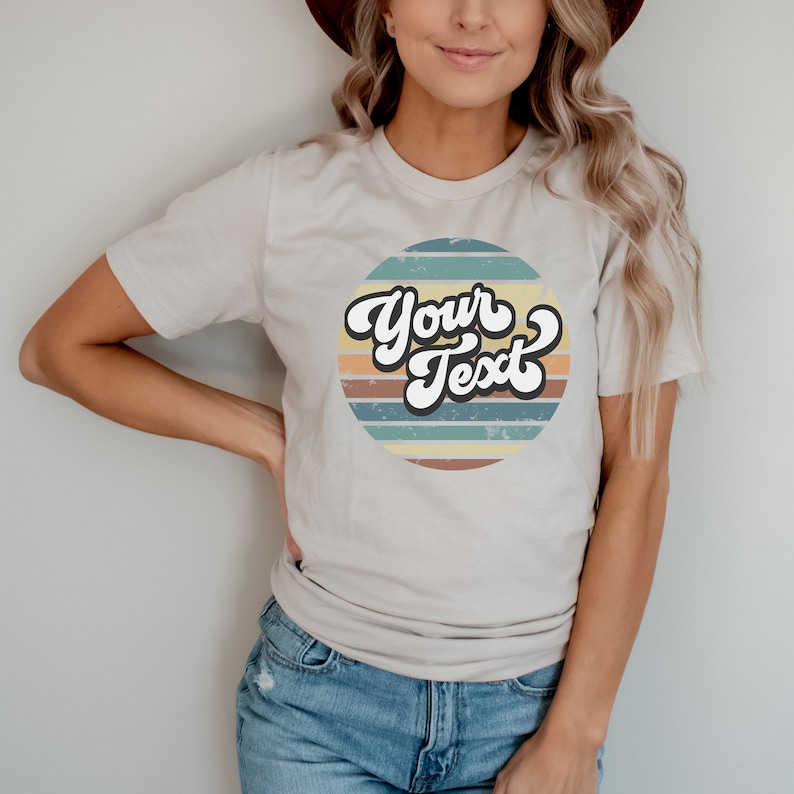 Puede incluir: Una camiseta blanca con un dise&ntilde;o gr&aacute;fico retro que presenta un c&iacute;rculo con rayas de colores y el texto "Your Text" en una fuente vintage.