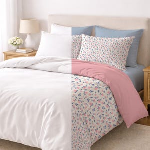 May include: A bed with white, pink, and floral bedding. The duvet cover is white on one side and pink on the other. Two pillows have a floral pattern with pink flowers and blue leaves. The bed also has a light blue sheet and white pillowcases.