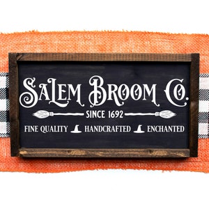 Peut inclure: Une enseigne en bois noir avec des lettres blanches qui disent "Salem Broom Co. Since 1692" avec un balai et un chapeau de sorci&egrave;re en graphique de chaque c&ocirc;t&eacute; du texte. L'enseigne dit &eacute;galement "Fine Quality", "Handcrafted", et "Enchanted" avec un chapeau de sorci&egrave;re en graphique entre chaque mot.