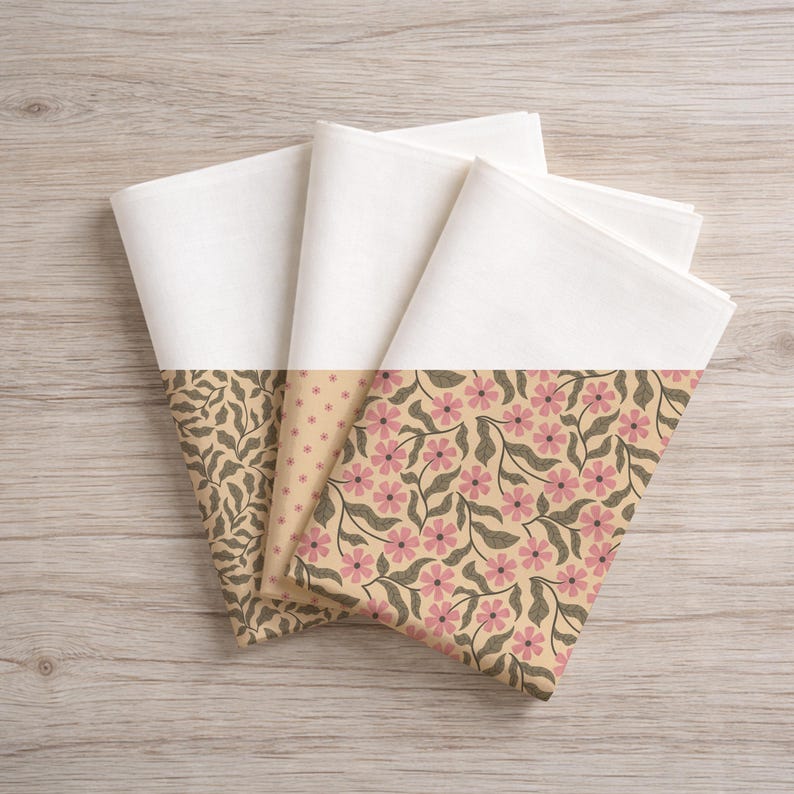 May include: Four folded white cloth napkins with patterned borders. The borders feature three different designs: a leafy pattern in brown, a dotted pattern in beige, and a floral pattern with pink flowers and green leaves on a beige background.