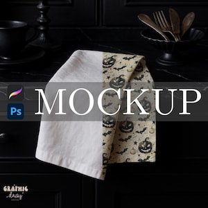 Pode incluir: Uma toalha de cozinha dobrada com tema de Halloween. Um lado é branco liso, o outro apresenta um padrão de abóboras, morcegos e estrelas em um fundo bege. A palavra "MOCKUP" é exibida na toalha.