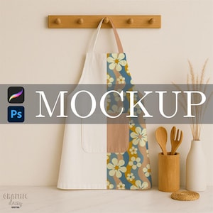 May include: A white and patterned apron with a pocket hangs from a wooden rack. The apron features a floral design in shades of blue, yellow, and brown. The word "MOCKUP" is displayed across the center of the image.