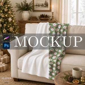 Peut inclure: Un plaid doux drapé sur un canapé, présentant une face blanche et une face verte avec un motif répétitif de visages de Père Noël, de feuilles de houx et de petits points blancs. Le plaid est présenté dans une pièce avec une décoration de Noël.