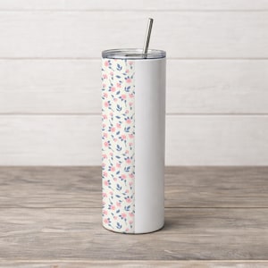 May include: A white stainless steel tumbler with a floral pattern of pink roses and blue leaves on a cream background. The tumbler has a silver lid and a silver straw. The tumbler is cylindrical and sits on a wooden surface.