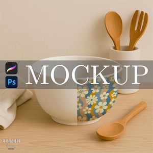 Può includere: Una ciotola in ceramica bianca con un motivo floreale blu, arancione e crema. La parola "MOCKUP" è sovrapposta alla ciotola. Cucchiaini e una forchetta di legno sono in un supporto bianco e un cucchiaino di legno è appoggiato sul tavolo.
