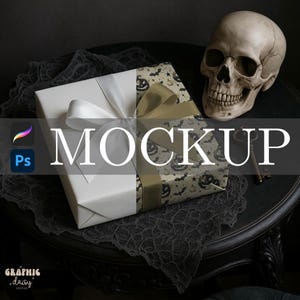 以下が含まれることがあります： ハロウィーンをテーマにしたモックアップ。白い紙と模様入りの紙で包まれ、リボンで飾られた2つのギフトボックス。骸骨と鍵が、装飾的な布が敷かれた暗いテーブルの上に置かれています。「MOCKUP」という文字が画像に重ねられています。