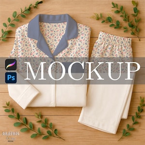 May include: A two-piece pajama set with a floral print top and solid cream-colored pants. The top has a blue collar and cuffs. The word "MOCKUP" is displayed across the center of the image. Green leaves are arranged around the pajamas.