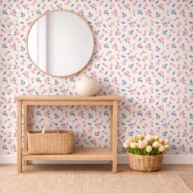May include: A light wood console table with a woven basket on the lower shelf. A round mirror hangs above the table. The wall is covered in a floral pattern with pink flowers and blue leaves. A vase sits on the table.