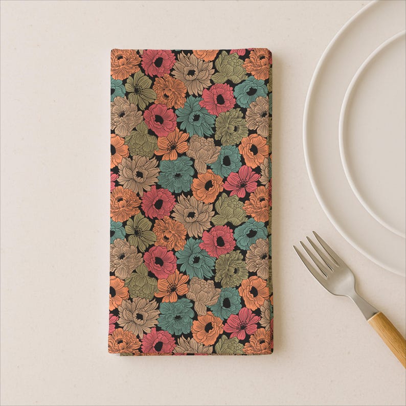 Puede incluir: Una servilleta rectangular floral con fondo negro. La servilleta est&aacute; cubierta con un patr&oacute;n de flores coloridas en tonos naranja, rosa, turquesa y beige. Un plato blanco y un tenedor con mango de madera est&aacute;n en el fondo.