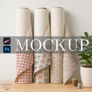 May include: Three rolls of patterned fabric, including gingham, bows, and floral designs. The word "MOCKUP" is displayed across the image. A small potted plant, spools of thread, and a thimble are on the wooden surface.