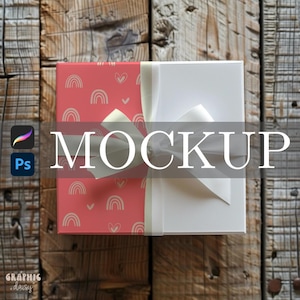 May include: A gift box mockup with a red patterned lid featuring rainbows and hearts, and a white box section. The box is tied with a cream-colored ribbon. The word "MOCKUP" is displayed across the box.