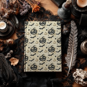 May include: A hardcover journal with a Halloween-themed pattern featuring jack-o'-lanterns, bats, and stars on a cream background. The journal is surrounded by decorative items, including a candle, feather, and dried flowers, creating a spooky aesthetic.