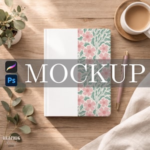 May include: A notebook with a floral design and the word "MOCKUP" in large white letters. The notebook is on a wooden surface, with a pen, a cup of coffee, and a small plant nearby.