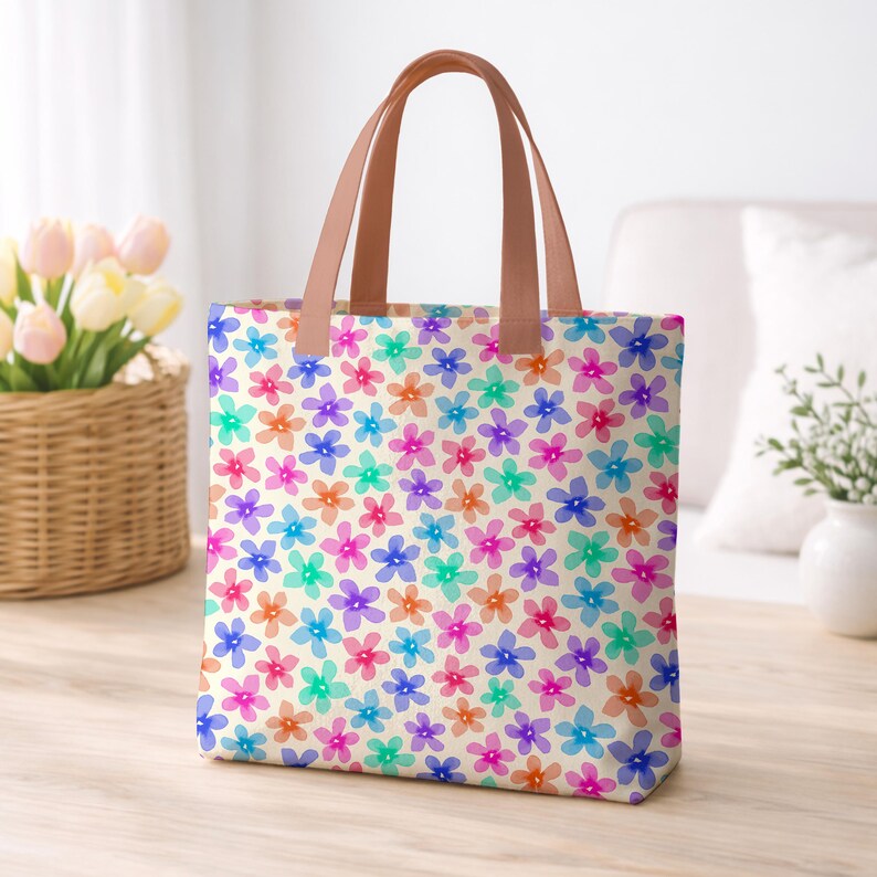 May include: A floral tote bag with a cream background and a pattern of colorful flowers in shades of pink, orange, blue, purple, and green. The bag has brown handles.