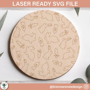 Peut inclure: Un design rond en bois sur le thème de Pâques avec des illustrations découpées au laser de lapins, de carottes et de tulipes. Le texte "LASER READY SVG FILE" est en haut. Le design est brun clair avec un grain de bois naturel.