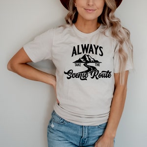 May include: A white t-shirt with a black graphic that says "Always Take The Scenic Route" with a mountain and road design.