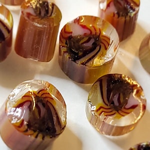 Puede incluir: Surtido de cuentas redondas de vidrio transparente con un patrón de espiral en tonos marrones, amarillos y blancos.