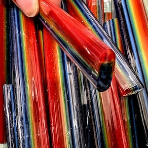 May include: Close-up of a bundle of colorful glass rods with a rainbow iridescent effect. The rods are arranged vertically and have a smooth, polished finish.