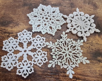 Puede incluir: Cuatro adornos de copo de nieve blancos con detalles de purpurina. Los copos de nieve están hechos de un material ligero y tienen diseños intrincados.