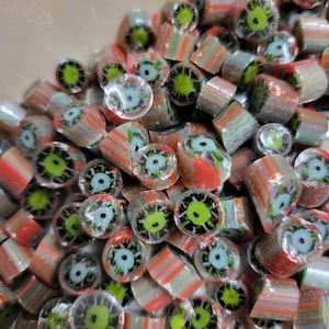 May include: A pile of colorful, eye-shaped hard candies. The candies have a clear, striped exterior with a central design featuring a green iris, blue pupil, and black details. The candies are a mix of red, gray, and clear colors.