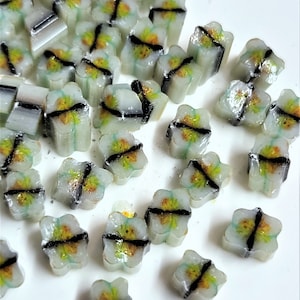 Könnte beinhalten: Eine Sammlung kleiner, weißer Glasfliesen mit einem schwarzen und gelben Blumendesign. Die Fliesen sind auf einer weißen Oberfläche verstreut.