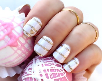 May include: White nail polish with gold glitter stripes. The nails are short and rounded. The nails are decorated with a small gold heart on one nail.
