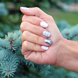 May include: A hand with light blue and white checkered nail polish and a white nail with a gray deer silhouette.