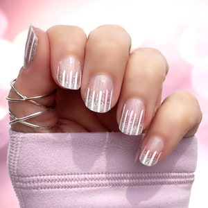 May include: Close-up of a hand wearing pink and white nail wraps with silver glitter accents. The nail wraps feature a vertical stripe design.