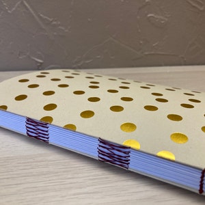 May include: A white notebook with gold polka dots and a burgundy thread binding.