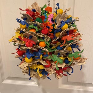 May include: A colorful bird toy for parrots and other birds. The toy is made of natural woven material and features a variety of plastic toys, including balls, rings, and figures. The toy is attached to a metal chain for hanging.