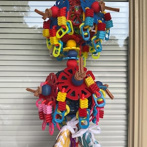 May include: A hanging bird toy featuring two spherical structures adorned with colorful plastic components, including red, yellow, and blue rings, beads, and connectors. The toy includes two miniature canvas sneakers in yellow and light blue.