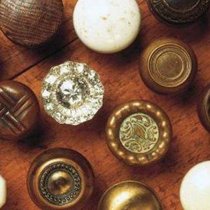 May include: A collection of antique door knobs in various styles and materials, including wood, brass, and crystal. The knobs are arranged on a wooden surface, showcasing their unique designs and textures.