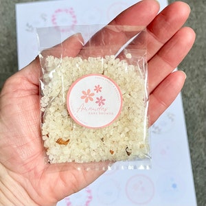 May include: A small clear plastic bag filled with white bath salts with a pink and white sticker that says "Amanda's Baby Shower" with pink flowers. The sticker also says "Calming & Relaxing" and "Enjoy Your Moment".