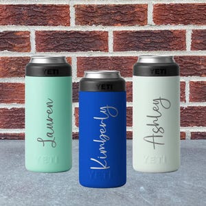 May include: Three insulated beverage holders in mint green, blue, and white, each with a black top and the brand name "YETI". The holders are personalized with the names "Lauren", "Kimberly", and "Ashley" in a cursive font.