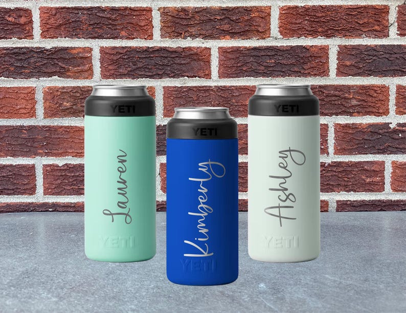 May include: Three insulated beverage holders in mint green, blue, and white, each with a black top and the brand name "YETI". The holders are personalized with the names "Lauren", "Kimberly", and "Ashley" in a cursive font.