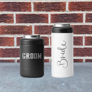May include: Two insulated beverage holders, one black and one white, with silver rims. The black holder has "Groom" in silver lettering, and the white holder has "Bride" in cursive. Both have the "YETI" logo.